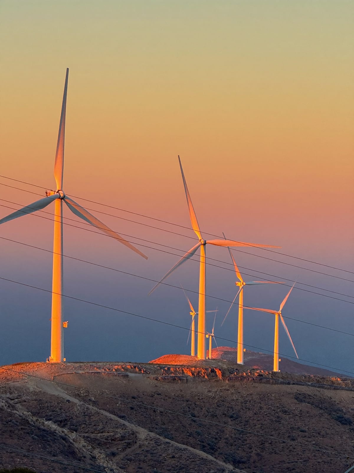 Wind turbines on a Greek island ridge at dusk with transmission lines